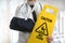 Doctor Wearing Elbow Sling Holding Caution Sign