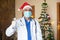 Doctor wearing mask and christmas santa hat doing thumb up, healthcare medical person on duty celebration during covid-19 pandemic