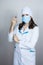 Doctor in white coat with dark hair in medical blue mask holds syringe in hands on light background