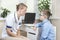 Doctor in a white coat and a stethoscope around the neck is sitting in the doctor`s office. He talks to the boy in a blue shir