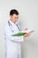 A doctor in a white coat with a stethoscope on his neck reads tests in a green folder. One on a white background