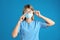 Doctor wiping foggy glasses caused by wearing disposable mask on blue background. Protective measure during coronavirus pandemic