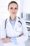 Doctor woman headshot at work in hospital. Physician standing straight and smiling, studio portrait. Medicine and health