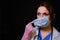 A doctor with wounds on his face takes off a medical mask. Nurse on a black background with mask marks, closeup. Concept of