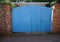 Dog peeks out under large blue wooden gate