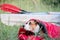 A dog rests in a sleeping bag in front of a canoe boat at camping site.