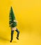 The doll carries a toy Christmas tree on a yellow background with copy space