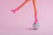 Doll feet on a small disco ball on a pink background