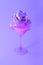 A doll lying in a glass filled with a pink neon drink. Illuminated by purple neon light. Gray foil for resting over the eyes on a