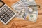 Dollars, calculator, wristwatch on a wooden background. View from above.