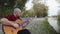 Dolly in shot of an alternative man sitting at park and playing guitar