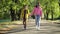 Dolly shot of happy carefree loving teenage couple strolling in sunshine on park alley holding hands. Cheerful positive