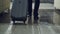 Dolly shot of legs of businessman walking through hotel lobby pulling luggage and stop at reception desk. Business