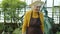 Dolly shot of senior woman gardener walking in greenhouse looking at plants smiling