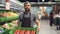 Dolly shot of young salesman in apron carrying box of tomatoes in supermarket in fruit and vegetables department