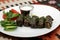 Dolma, sarma, stuffed grape leaves. On a white platter with sour cream and vegetables. On a tablecloth with a national ornament