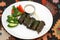 Dolma, sarma, stuffed grape leaves. On a white platter with sour cream and vegetables. On a tablecloth with a national ornament