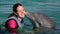 Dolphin kiss young woman in blue water. Smiling woman swimming with dolphin.