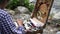 Dombay, Russia 26 July 2020: Close up of young woman drawing picture on cardboard on hike. Paintress depicting mountain