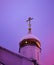 The dome of the church with a cross is lit by pink and purple flowers of dawn. Russia