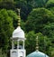 Dome of a mosque with a minaret surrounded by lush green forest and trees in South India