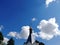 Dome of the Russian Orthodox Church with a cross against the blue sky and white clouds.  Near the tops of the trees.