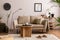 Domestic and cozy interior of living room with beige sofa, plants, shelf, coffee table, boucle rug, mock up poster frame, side