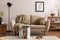 Domestic and cozy interior of living room with beige sofa, plants, shelf, coffee table, boucle rug, mock up poster frame, side