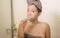 Domestic lifestyle portrait of young happy and beautiful Asian Chinese woman brushing her teeth wearing head towel wrap at