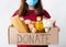 Donate box with food, foodstuffs in female hands on white background. Volunteer in protective mask make food delivery during covid