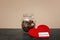 Donation jar with coins and red heart on table