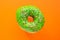 Donut green with sprinkles isolated on orange background, close-up