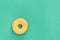 Donut with yellow glaze on green background. Top view