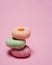 Donuts with different colors stacked into one isolated on a pink background.