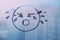 doodle drawn sad face on foggy glass window raindrops blue color concept photo