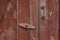 The door of the old village toilet is closed with a swing bolt. A revolving shutter for a red wooden door with scuffed paint.