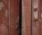 The door of the old village toilet is closes with a swing bolt. A revolving shutter for a red wooden door with scuffed paint.