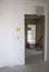 Doorway in renovated room,white primed wall on side,corridor and another room,dirty vacuum cleaner on floor,garbage