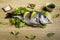 Dorada fresh fish on lettuce leaves next to some bay leaves, some pieces of lemon, a bowl of oil and some spices on a wooden table