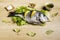 Dorada fresh fish on lettuce leaves next to some bay leaves, some pieces of lemon, a bowl of oil and some spices on a wooden table