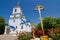 Dormition of the Mother of God russian Orthodox church, temple and crucifix cross in churchyard, red roses orchard