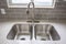 Double bowl stainless steel sink undermounted on the white kitchen countertop