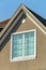 Double gable roof with brown stucco exterior with red brick roof tiles and window with white accent color