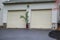 Double overhead garage doors with a potted palm tree in between the doors at the end of as asphalt driveway.