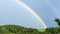 Double rainbow on a gray sky after rain. A rare atmospheric phenomenon after a storm. Beautiful hilly landscape with a real