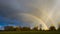 Double rainbow passing through rain shafts above rural countryside