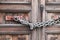 A double wooden door chained closed. Closeup of old wooden door with closed padlock on a chain. A chain of silver color