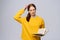 Doubtful dissatisfied young woman college student wearing yellow sweater looking at camera holding book