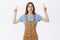 Doubtful and hesitant cute unimpressed girlfriend in brown overalls over t-shirt raising hands pointing up and smirking