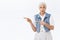 Doubtful, skeptical, indecisive senior woman, grey hair, wear denim vest, dress, pointing left and look camera hesitant